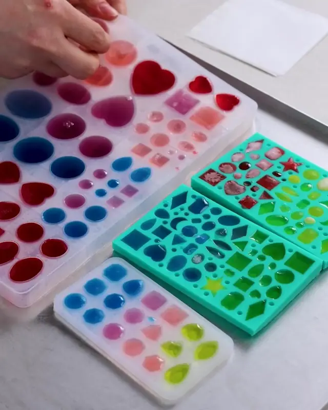 Molds filled with red, blue, pink, and green gelatin on a tray