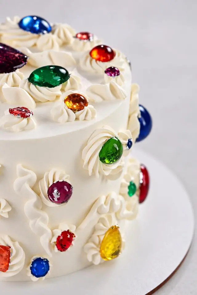 White cake with piped ruffles and colorful edible gems