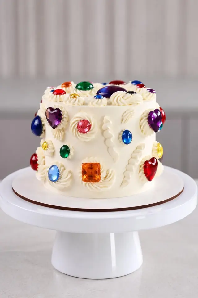 Small white cake with simple piping and a few edible gems