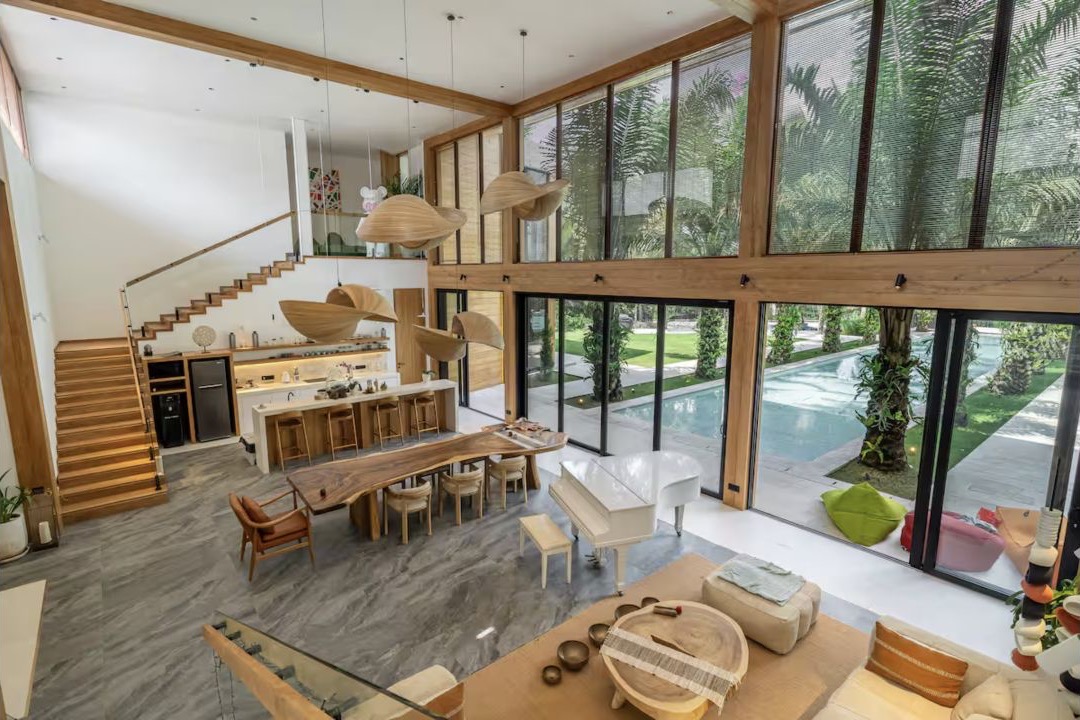 Double-height living room, kitchen, piano, and pool view inside Dmitry's Bali villa