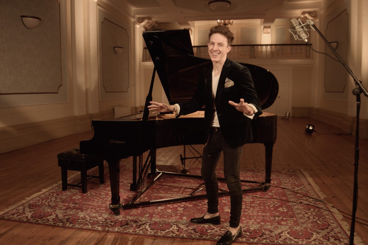 Stephen Ridley standing at an open grand piano, mid explanation