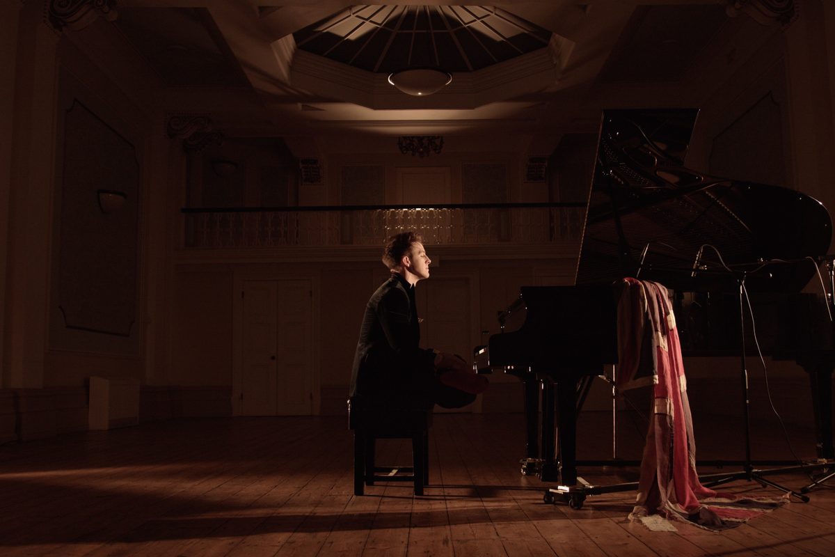Stephen Ridley alone at the grand piano in an empty hall