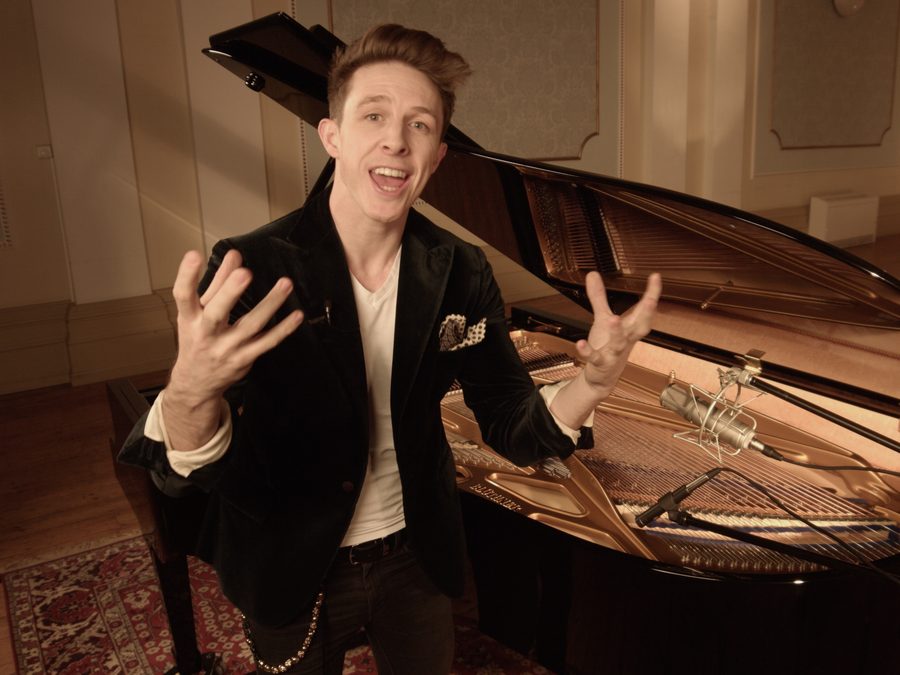 Stephen Ridley explaining something with both hands, standing at an open grand piano